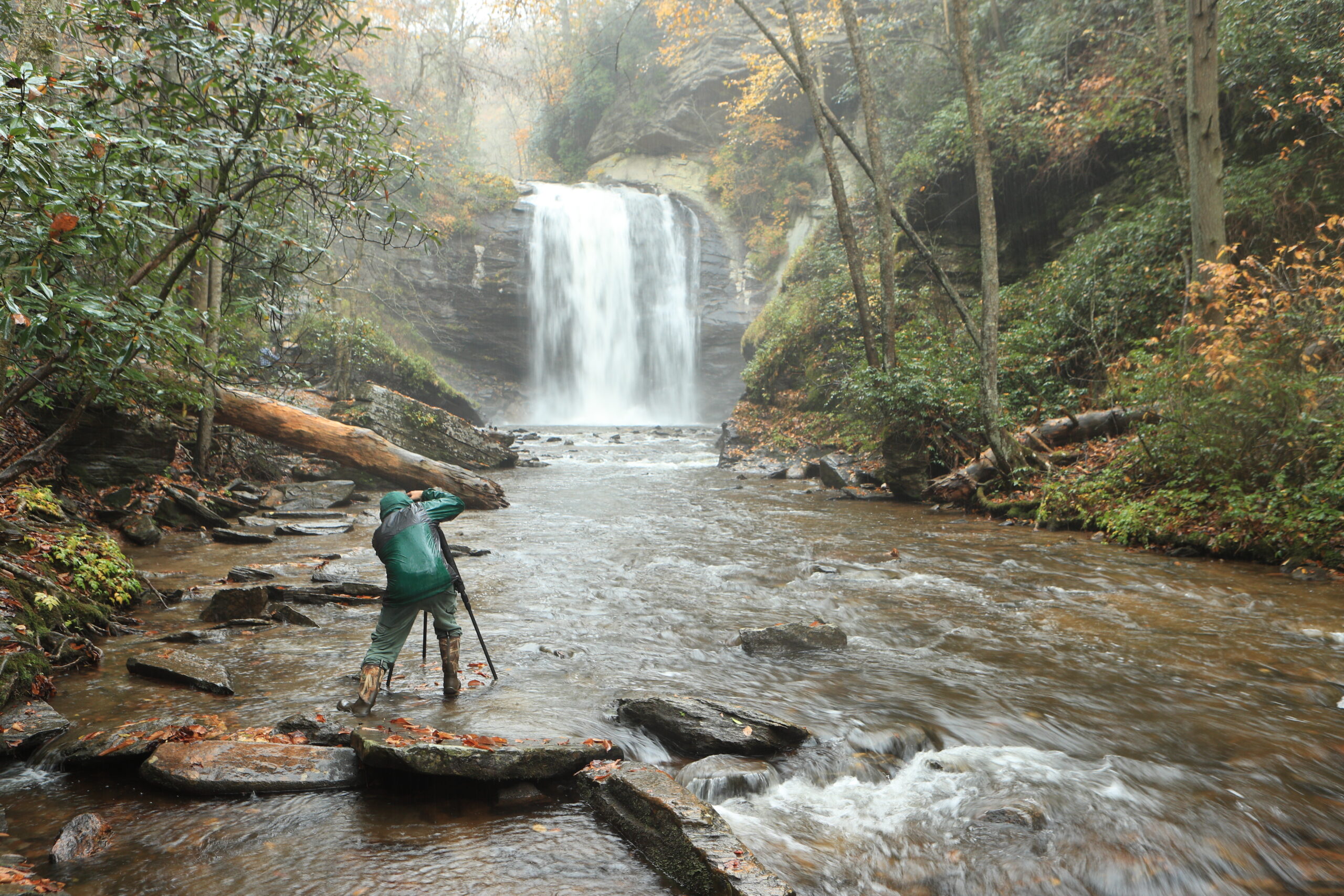 Photographer with tripod standing in river taking picture of waterfall.