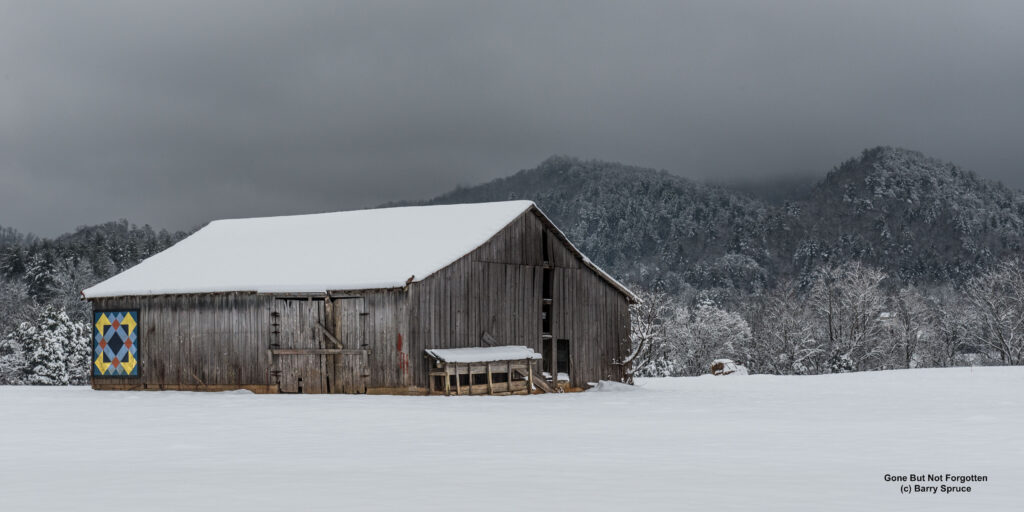 Barn in snowy field with colorful quilt pattern on side.